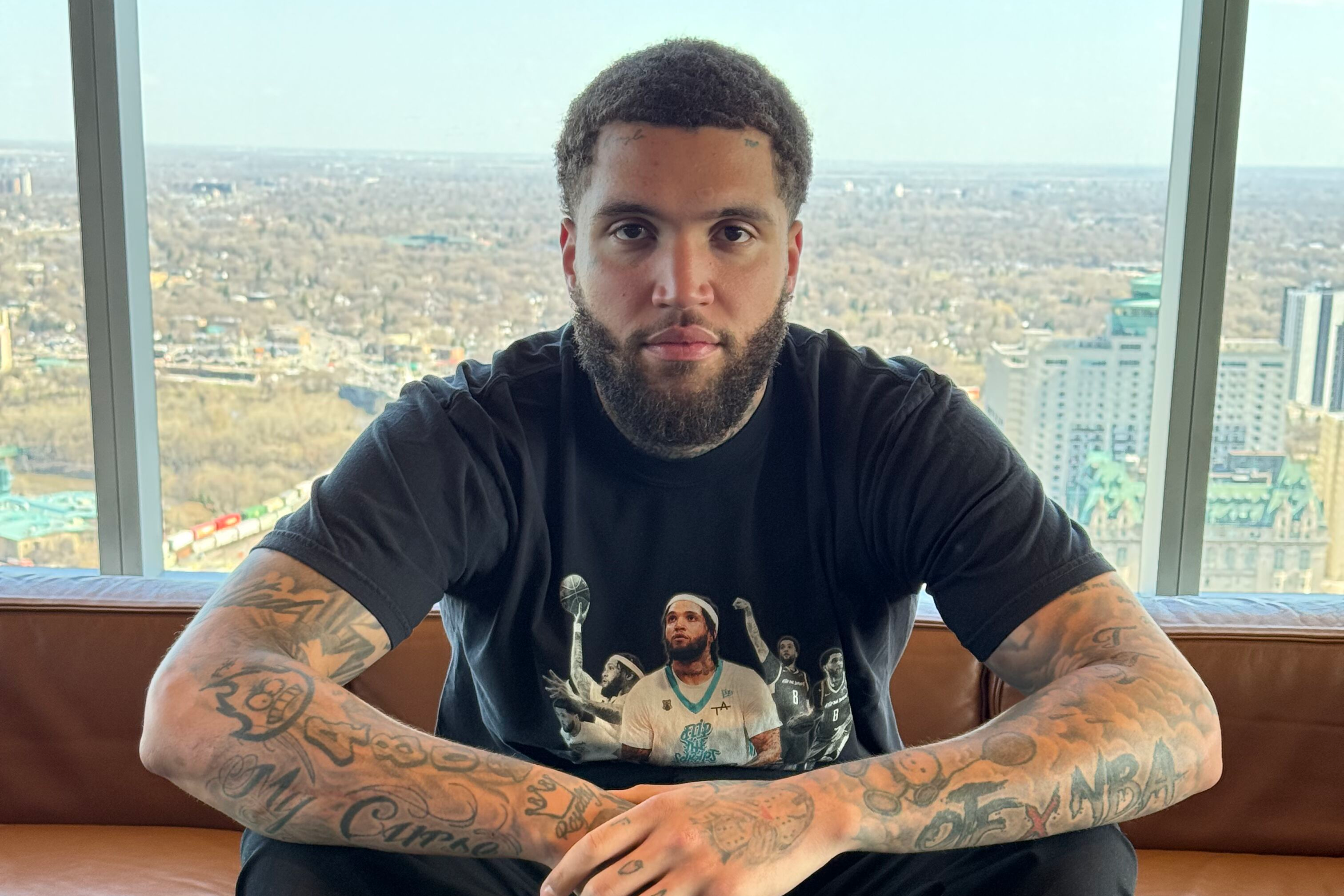 Man with tattoos sitting on a couch with a cityscape view